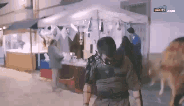 a man in a military uniform is walking down a street in front of a market stall .