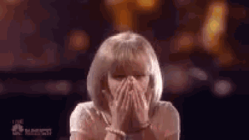 a woman with blonde hair is covering her face with her hands while standing in front of a crowd .