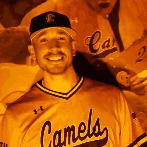 a man wearing a camels jersey smiles in front of a poster