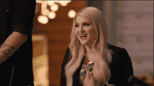 a woman with blonde hair and a black jacket is smiling while sitting at a table .