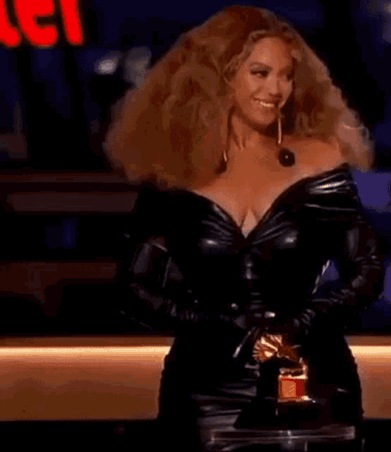 beyonce is wearing a black leather dress and gloves and holding a trophy .