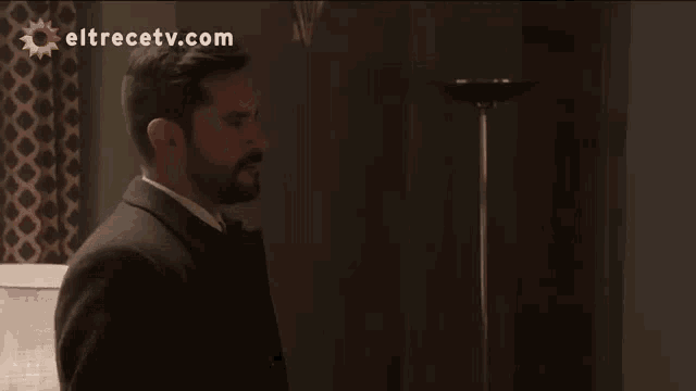 a man in a suit and tie is standing in a dark room with eltrecetv.com written on the bottom