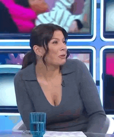 a woman with a plunging neckline is sitting at a table with a glass of water in front of her .
