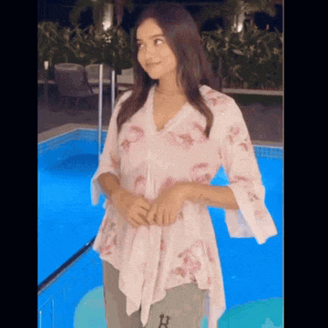 a woman is standing in front of a swimming pool wearing a floral shirt .