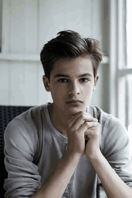 a young man with his hands on his chin looks at the camera