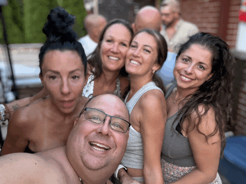 a group of people posing for a picture including a shirtless man wearing glasses