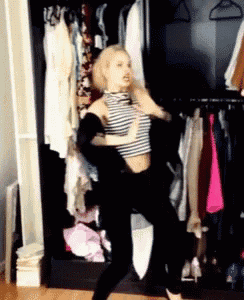 a woman in a striped top is dancing in a closet full of clothes