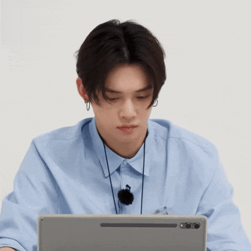 a young man wearing a blue shirt is sitting in front of a laptop computer