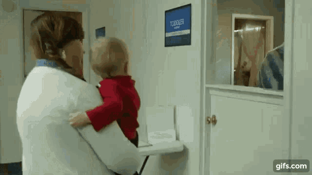 a woman is holding a small child in front of a sign that says toddler room .