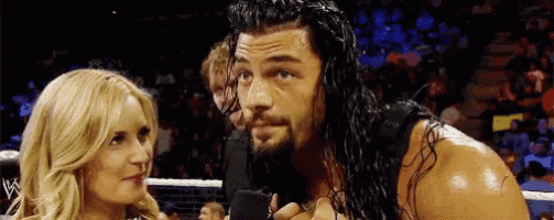 roman reigns is talking into a microphone while a woman looks on .