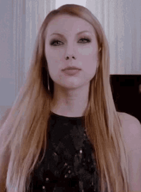 a woman with long blonde hair and a black dress is looking at the camera .