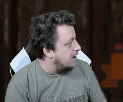 a man with curly hair and a beard is sitting in a chair with his mouth open .