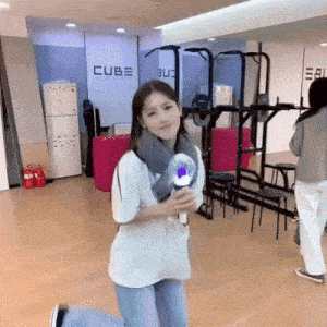a woman in a white shirt is holding a light stick in front of a wall that says cube