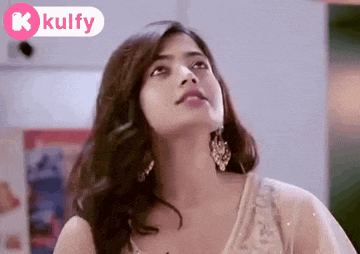 a woman in a white dress and earrings is looking up at something .
