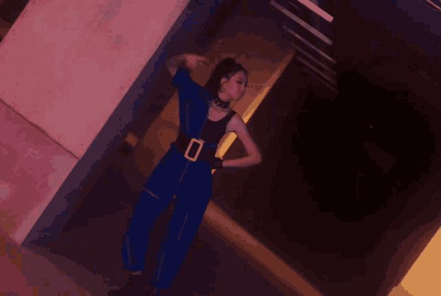 a woman in a blue jumpsuit is leaning against a concrete wall