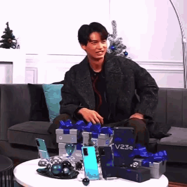 a man is sitting on a couch next to a table with gifts and phones .