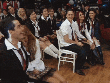 a group of people in school uniforms are sitting in chairs and laughing