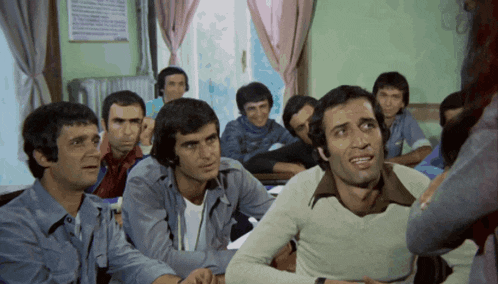a group of men are sitting in a classroom with one man making a face