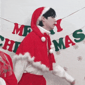 a man dressed as santa claus is dancing in front of a merry christmas banner .