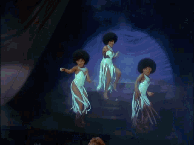 three women in white dresses are dancing on stage