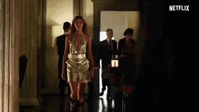 a woman in a gold dress and cowboy boots is walking down a hallway with a netflix logo in the background .