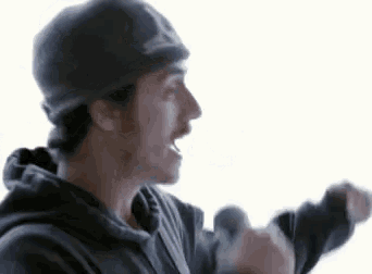 a man wearing a hat and a hoodie is standing in front of a white background and screaming .