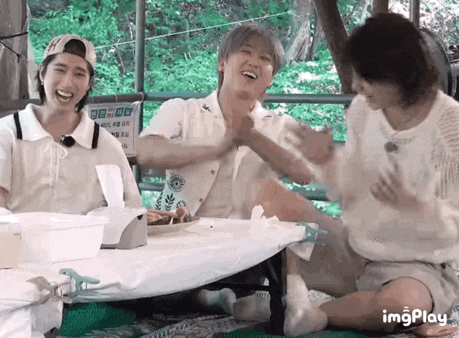a group of people are sitting at a table laughing and giving each other high fives .