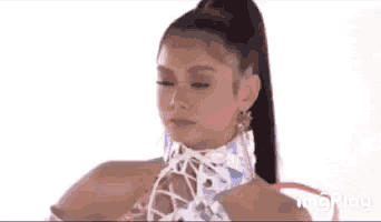a woman with a ponytail is wearing a white lace up top and earrings .