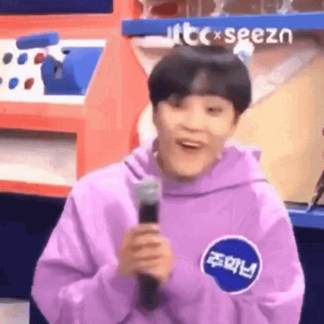 a young man in a purple hoodie is holding a microphone .