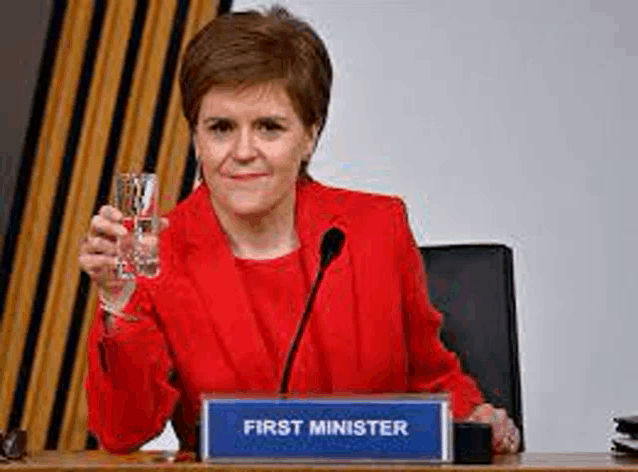a woman in a red jacket is sitting at a table with a microphone holding a glass of water .