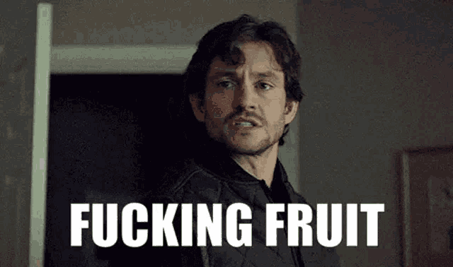 a man with a beard is standing in front of a door with the words `` fucking fruit '' written on it .