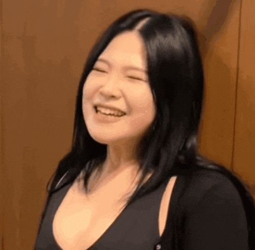 a woman with long black hair is smiling with her eyes closed and her mouth open .