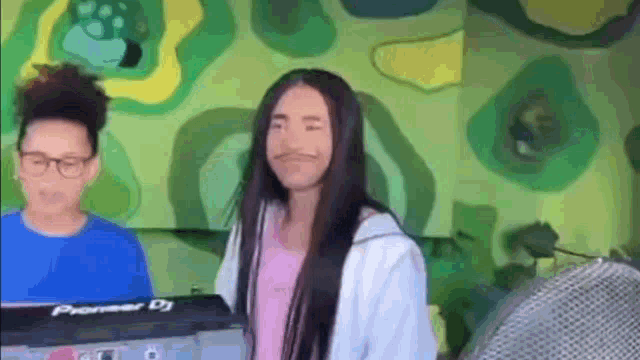 a woman with long hair and a mustache is standing in front of a pioneer dj controller .
