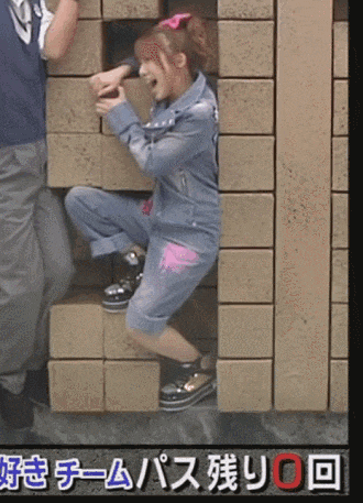 a girl in a denim jacket is squatting down in front of a wall of bricks