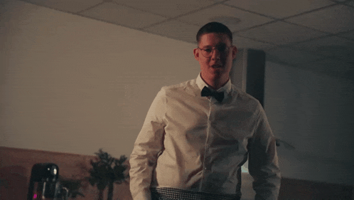 a man in a white shirt and bow tie adjusts his belt