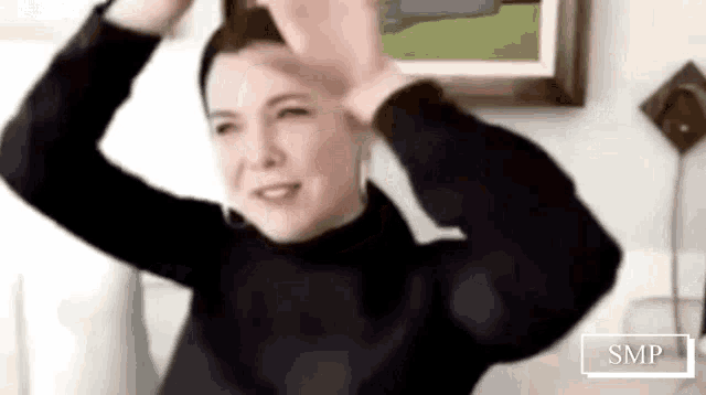 a woman in a black turtleneck sweater is dancing in front of a framed picture .
