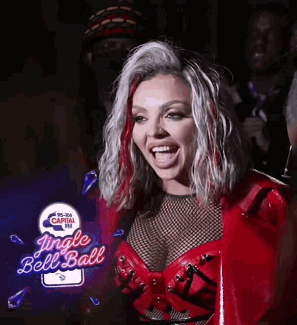a woman in a red outfit is smiling in front of a jingle bell ball sign