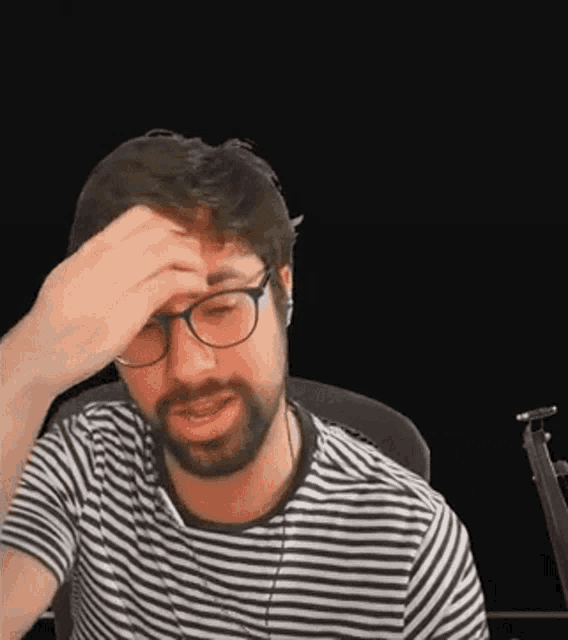 a man with a beard and glasses is holding his head .