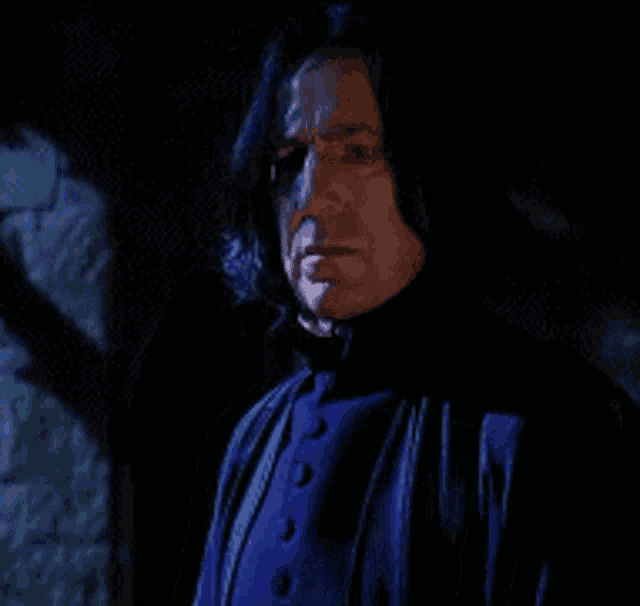 a man with long hair and a blue jacket is standing in the dark