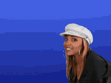 a woman wearing a white hat and earrings smiles for the camera