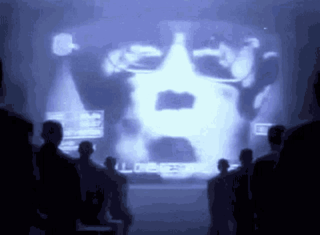 a group of people are looking at a large screen with a picture of a man 's face on it