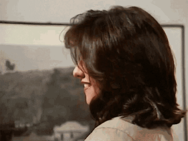 a woman with long dark hair is smiling in front of a painting .