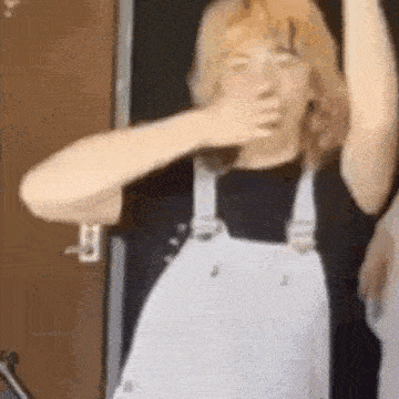 a person wearing white overalls is covering their mouth with their hand .