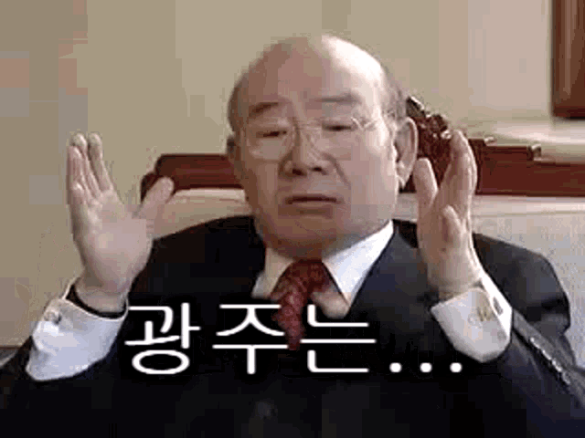 an elderly man in a suit and tie is sitting in a chair with his hands up .