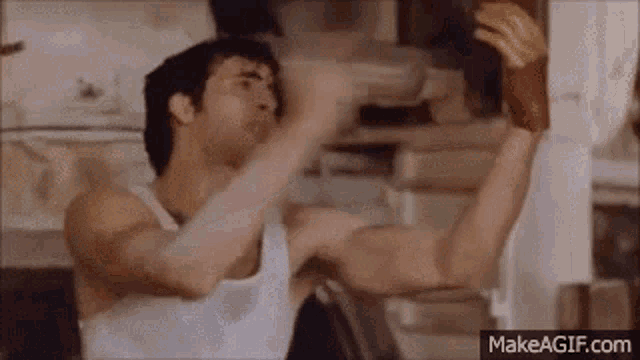 a man in a white tank top is flexing his muscles while holding a glove .