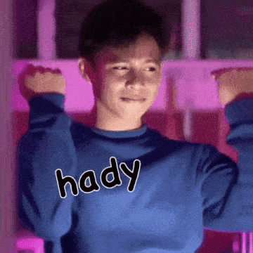 a young boy wearing a blue sweater with the word hady on it is flexing his muscles .
