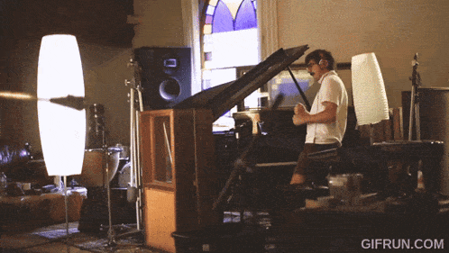 a man playing a piano in a room with gifrun.com written on the bottom right
