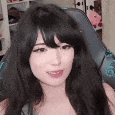 a woman with long black hair and bangs is sitting in a gaming chair and smiling .
