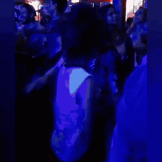 a woman in a white tank top is dancing in a dark room