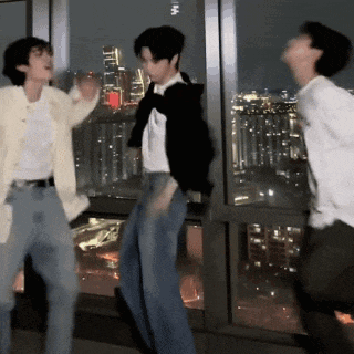 three people are dancing in front of a window with a view of the city at night